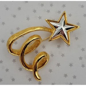 May include: A gold and silver tone brooch featuring a stylized shooting star with a swirling tail.