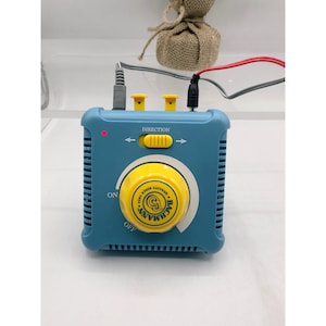 Puede incluir: Un controlador de potencia para trenes Bachmann de color turquesa con un gran dial amarillo y el texto "Bachmann Quality Since 1853". Tiene un interruptor de dirección y conectores de entrada. Diseñado para trenes modelo.