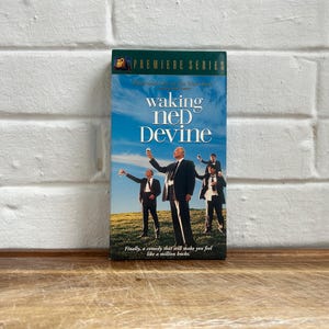 May include: A VHS tape of the movie "Waking Ned Devine" with a blue sky background and a group of men in suits. The title is in white, and the tape is labeled "Premiere Series."