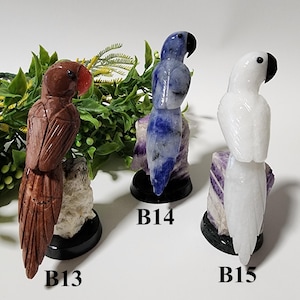 Pode incluir: Três estatuetas de papagaio em pedra esculpida. Uma é marrom com bico vermelho, outra azul com detalhes pretos e a terceira branca com bico preto. Cada papagaio é montado em uma base.