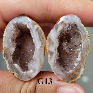 Puede incluir: Dos mitades de una geoda con un exterior blanco y un interior marrón lleno de cristales de cuarzo transparentes. La geoda está etiquetada como "G13".