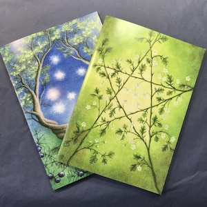 May include: Two rectangular greeting cards featuring detailed illustrations. One card displays a night scene with a tree and glowing stars against a blue sky. The other card shows a bright green background with white flowers arranged in a star shape.