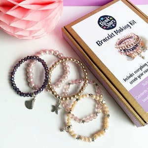 Könnte beinhalten: Ein Set aus vier Armbändern mit unterschiedlich farbigen Perlen und Charms. Die Armbänder befinden sich in einer Schachtel mit der Aufschrift "Bead Stars Bracelet Making Kit".