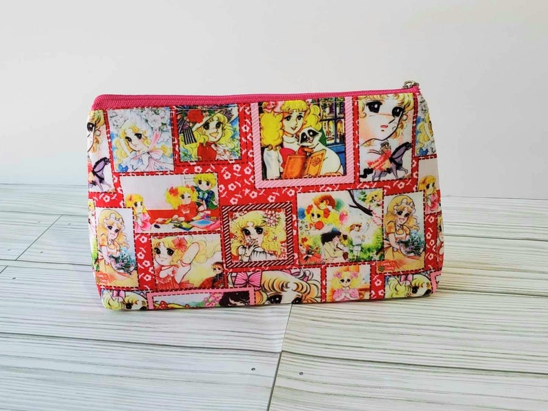May include: Pink zippered pouch with a colorful print of cartoon girls in various scenes. The print features a red, white, and pink color scheme.