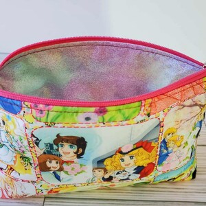 May include: A pink zippered pouch with a colorful floral print featuring cartoon characters. The pouch is open and the inside lining is pink.