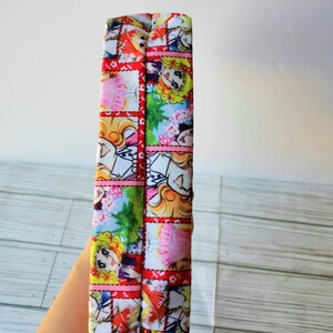May include: A red and white fabric pouch with a colorful cartoon print of girls and flowers. The pouch is folded in half and the seam is visible.