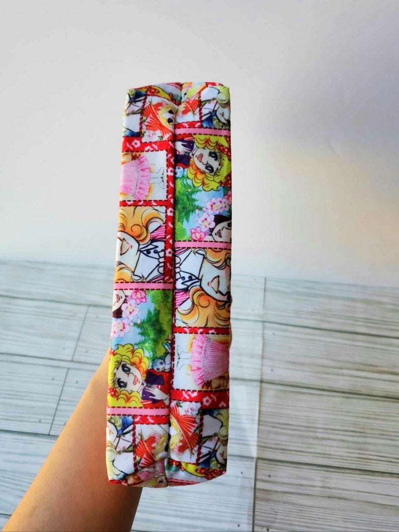 May include: A red and white fabric pouch with a colorful cartoon print of girls and flowers. The pouch is folded in half and the seam is visible.