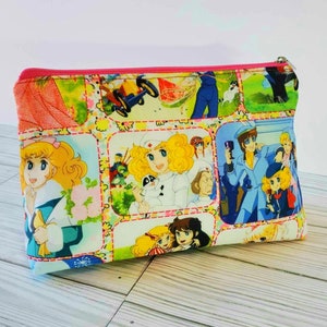 May include: A pink zippered pouch with a colorful patchwork design featuring cartoon characters and images. The pouch is made of fabric and has a white background with pink, blue, yellow, and green accents.