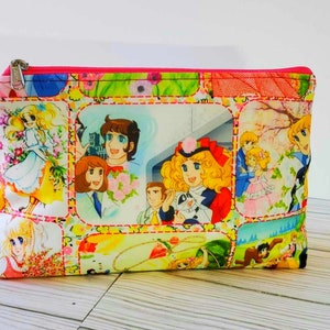 May include: A pink zippered pouch with a colorful print of cartoon characters from a Japanese anime series. The print features a variety of scenes with the characters in different settings.