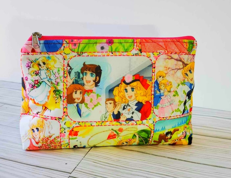May include: A pink zippered pouch with a colorful print of cartoon characters from a Japanese anime series. The print features a variety of scenes with the characters in different settings.
