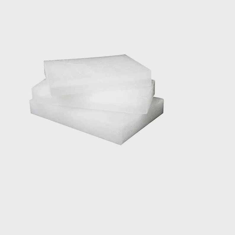 Puede incluir: Tres bloques de cera blancos y rectangulares apilados. Los bloques tienen una apariencia ligeramente transl&uacute;cida y est&aacute;n dispuestos en una composici&oacute;n simple sobre un fondo liso. La cera parece no tener perfume. Cada bloque mide aproximadamente 10 cm x 15 cm.