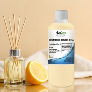May include: A clear glass bottle with a white cap filled with a yellow liquid. The bottle is labelled "GumDrop Australia Scented Reed Diffuser Refill". The bottle is sitting on a white cloth with a lemon slice next to it.