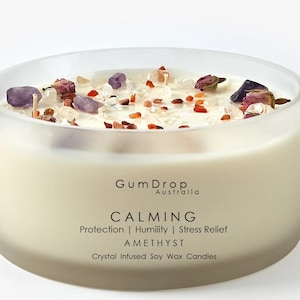Könnte beinhalten: Eine weiße Sojawachskerze mit Amethystkristallen, Rosenblüten und klaren Quarzkristallen. Die Kerze befindet sich in einem durchsichtigen Glasgefäß und trägt den Text "Gum Drop Australia" und "CALMING Protection | Humility | Stress Relief AMETHYST Crystal Infused Soy Wax Candles" auf dem Etikett.