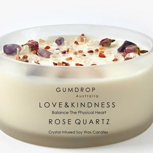 May include: A clear glass jar candle with a white soy wax base. The candle is topped with rose quartz crystals, rose petals, and red and white crystals. The label reads "GUMDROP Australia LOVE&KINDNESS Balance The Physical Heart ROSE QUARTZ Crystal Infused Soy Wax Candles".