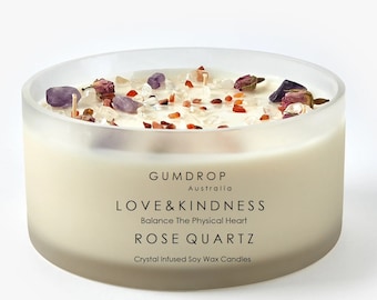 Puede incluir: Una vela de cristal transparente con una base de cera de soja blanca. La vela está cubierta con cristales de cuarzo rosa, pétalos de rosa y cristales rojos y blancos. La etiqueta dice "GUMDROP Australia LOVE&KINDNESS Balance The Physical Heart ROSE QUARTZ Crystal Infused Soy Wax Candles".