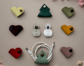 Puede incluir: Surtido de organizadores de cables de cuero de colores en varias formas, incluyendo corazones, un árbol de Navidad y muñecos de nieve. Los organizadores están diseñados para mantener los cables y los cables ordenados y organizados.