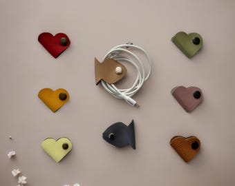 May include: Assortment of colourful leather cord organisers in heart and fish shapes. The organisers are designed to hold and manage cords and cables.