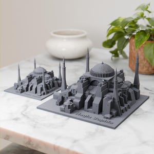 Può includere: Due modelli grigi della Hagia Sophia, una famosa moschea di Istanbul, in Turchia, stampati in 3D. I modelli sono su una superficie di marmo bianco. Il modello più grande è in primo piano e quello più piccolo è sullo sfondo.