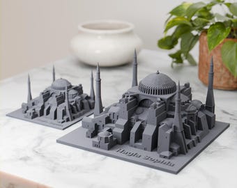 Puede incluir: Dos modelos grises de la Hagia Sophia, una famosa mezquita en Estambul, Turquía, impresos en 3D. Los modelos están sobre una superficie de mármol blanco. El modelo más grande está en primer plano y el más pequeño está en el fondo.