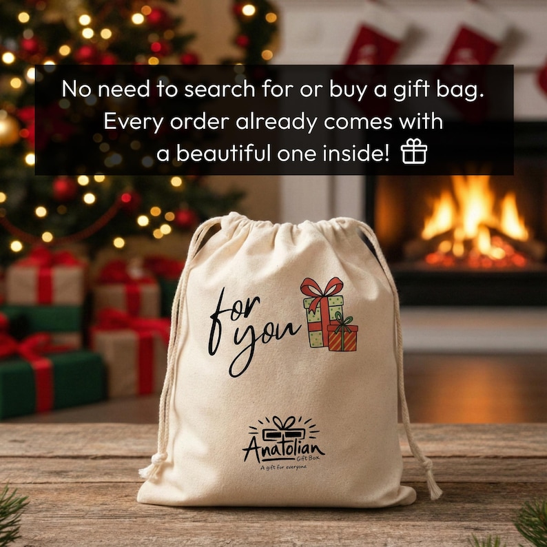A beige drawstring bag with a gift bag design sits on a wooden surface, with a fireplace and Christmas decorations visible in the background.