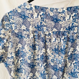 Puede incluir: Una blusa de estampado floral azul y blanco con cuello fruncido y mangas cortas.