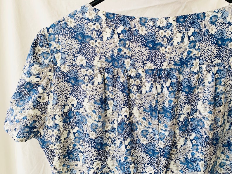 Puede incluir: Una blusa de estampado floral azul y blanco con cuello fruncido y mangas cortas.