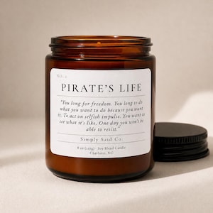 May include: A brown glass jar candle with a black lid. The label reads "PIRATE'S LIFE" with a quote about freedom. The candle is 8 oz (227g) and made with soy blend.