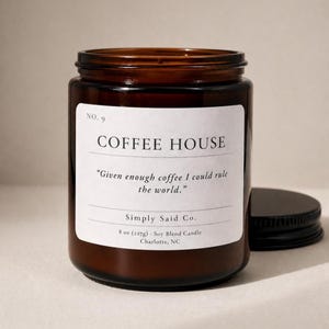 May include: A brown glass jar candle with a black lid. The label reads "COFFEE HOUSE" with the quote "Given enough coffee I could rule the world." It is an 8 oz (227g) soy blend candle.