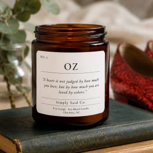 May include: A brown glass jar candle with a white label that reads "OZ" and a quote. The candle is 8 oz (227g) and is a soy blend. The candle is on a book with red shoes in the background.