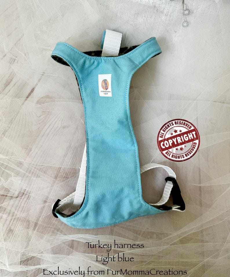 Pu&ograve; includere: Una pettorina per tacchino color azzurro con cinghie in nylon bianco e fibbie in plastica nera. Una piccola etichetta rettangolare del marchio &egrave; centrata sul pannello pettorale. Il testo "Turkey harness Light blue Exclusively from FurMommaCreations" &egrave; visibile.
