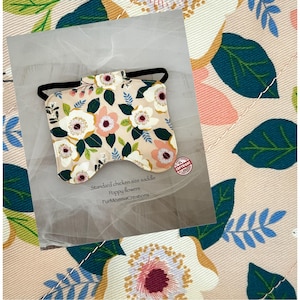 Pode incluir: Uma sela de galinha com um padrão floral de papoilas brancas e rosa, folhas verdes e uma faixa elástica preta. O texto no cartão diz "Standard chicken size saddle Poppy flowers".
