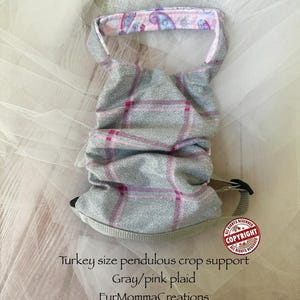 May include: A gray and pink plaid turkey size pendulous crop support with a light pink interior featuring a blue and purple paisley pattern. The item includes a beige adjustable strap with a black plastic buckle and text reading Turkey size pendulous crop support Gray/pink plaid FurMommaCreations.