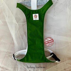 Pu&ograve; includere: Una pettorina per tacchino verde scuro con cinghie in nylon bianco e una fodera interna grigia. Una piccola etichetta quadrata con un logo colorato &egrave; centrata sul davanti. Il testo Turkey harness Dark Green FurMommaCreations &egrave; visibile.