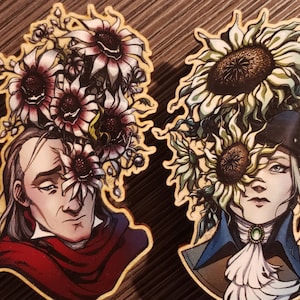May include: Two wooden ornaments featuring detailed illustrations of people with floral designs. The first ornament depicts a person with dark hair and a red scarf, surrounded by white and purple flowers. The second ornament depicts a person with light hair and a white collar, surrounded by yellow and green flowers. The text "Buy together for a discount!" is printed below the ornaments.