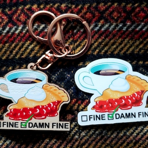 May include: A wooden keychain featuring a cartoon image of a cup of coffee and a slice of cherry pie. The text "FINE" is unchecked and "DAMN FINE" is checked.