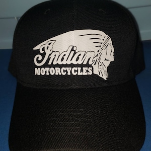 May include: Black baseball cap with a white Indian Motorcycles logo featuring a Native American headdress and the words "Indian Motorcycles".
