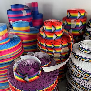 May include: A collection of colourful ribbon rolls with various rainbow patterns, including stripes, chevron, and geometric designs. The ribbons are arranged in stacks and are ready to be used for crafting, decorating, or gift wrapping.