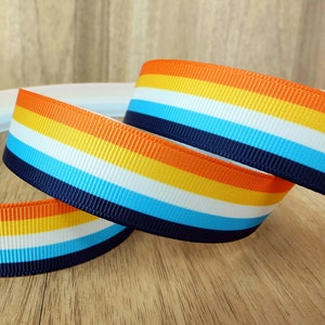Op de afbeelding: Gestroomd lint met oranje, gele, witte, blauwe en donkerblauwe strepen. Het lint is gevouwen in een lus.