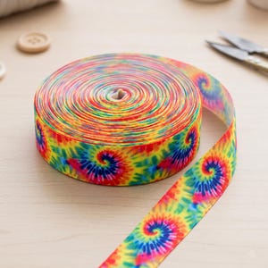 Może przedstawiać: Szpula wstążki rypsowej z żywym wzorem tie-dye w wirujących kolorach czerwonym, żółtym, niebieskim, zielonym i różowym. Wstążka ma wyraźną prążkowaną fakturę i jest zwinięta w ciasną, okrągłą szpulę na płaskiej powierzchni.