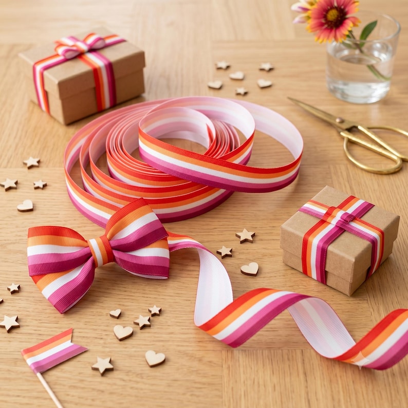Peut inclure: Plusieurs &eacute;l&eacute;ments de d&eacute;coration artisanale, dont un ruban enroul&eacute;, un n&oelig;ud et deux petites bo&icirc;tes cadeaux, tous avec un motif ray&eacute; rose, orange et blanc. Des &eacute;toiles et des c&oelig;urs en bois sont dispers&eacute;s. On aper&ccedil;oit &eacute;galement une paire de ciseaux dor&eacute;s et une petite fleur dans un verre.
