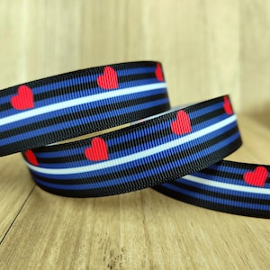 Puede incluir: Tres rollos de cinta rayada en negro, azul y blanco con corazones rojos impresos. La cinta es un símbolo de orgullo y amor.