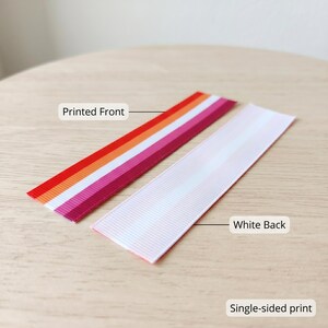 Peut inclure: Deux rubans, l'un avec un recto imprim&eacute; &agrave; rayures rouges, oranges, blanches et roses, et l'autre avec un verso blanc. Les textes "Printed Front", "White Back" et "Single-sided print" sont visibles.