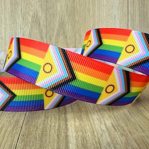 Puede incluir: Cinta de arcoíris con un patrón geométrico que presenta un triángulo marrón, rosa y blanco con un círculo amarillo en el centro. La cinta está doblada en tres.