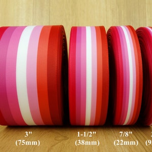 Op de afbeelding: Vier rollen gestreept grosgrain lint in rood, roze en wit. De breedtes variëren: 75mm, 38mm, 22mm en 9mm. De linten hebben verticale strepen.
