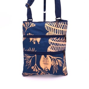 May include: Navy blue crossbody bag with a repeating pattern of beige botanical designs. The bag has three zippered compartments and an adjustable shoulder strap. The bag is made of a durable fabric.