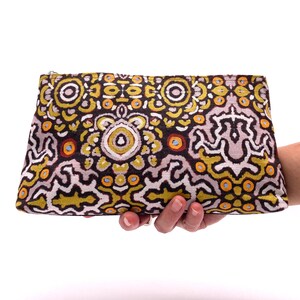 Op de afbeelding: Een zwarte ritszak met een kleurrijk geometrisch patroon in tinten geel, oranje, wit en bruin. Het patroon doet denken aan Aboriginal kunst.