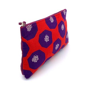 Op de afbeelding: Een rode en paarse ritszak met een geometrisch patroon van paarse zeshoeken met witte bloemmotieven.