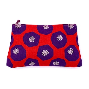Op de afbeelding: Een rode en paarse ritszak met een geometrisch patroon van paarse zeshoeken met witte bloemmotieven op een rode achtergrond.