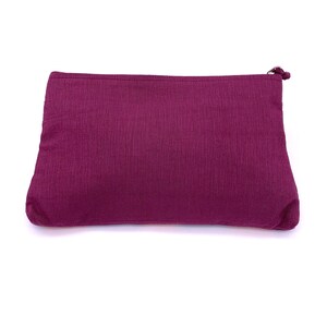 Op de afbeelding: Een diepe paarse, met rits gevulde tas gemaakt van een zachte, gestructureerde stof. De tas is gesloten en ligt plat op een wit oppervlak.