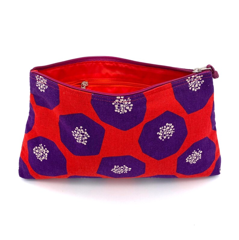 Op de afbeelding: Rode en paarse ritszak met een geometrisch patroon. De tas is open en de binnenkant is gevoerd met rode stof.
